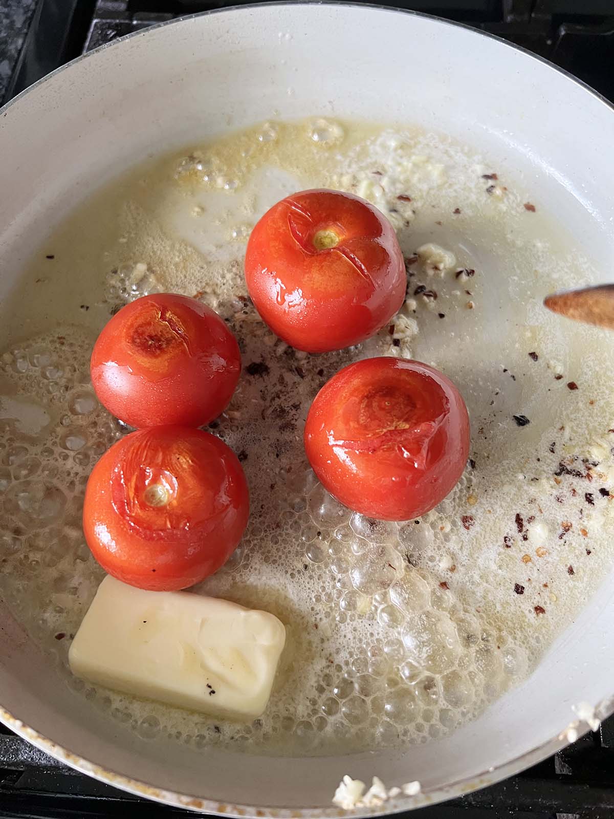 Tomatoes, butter, and red pepper flakes cooking in a skillet.