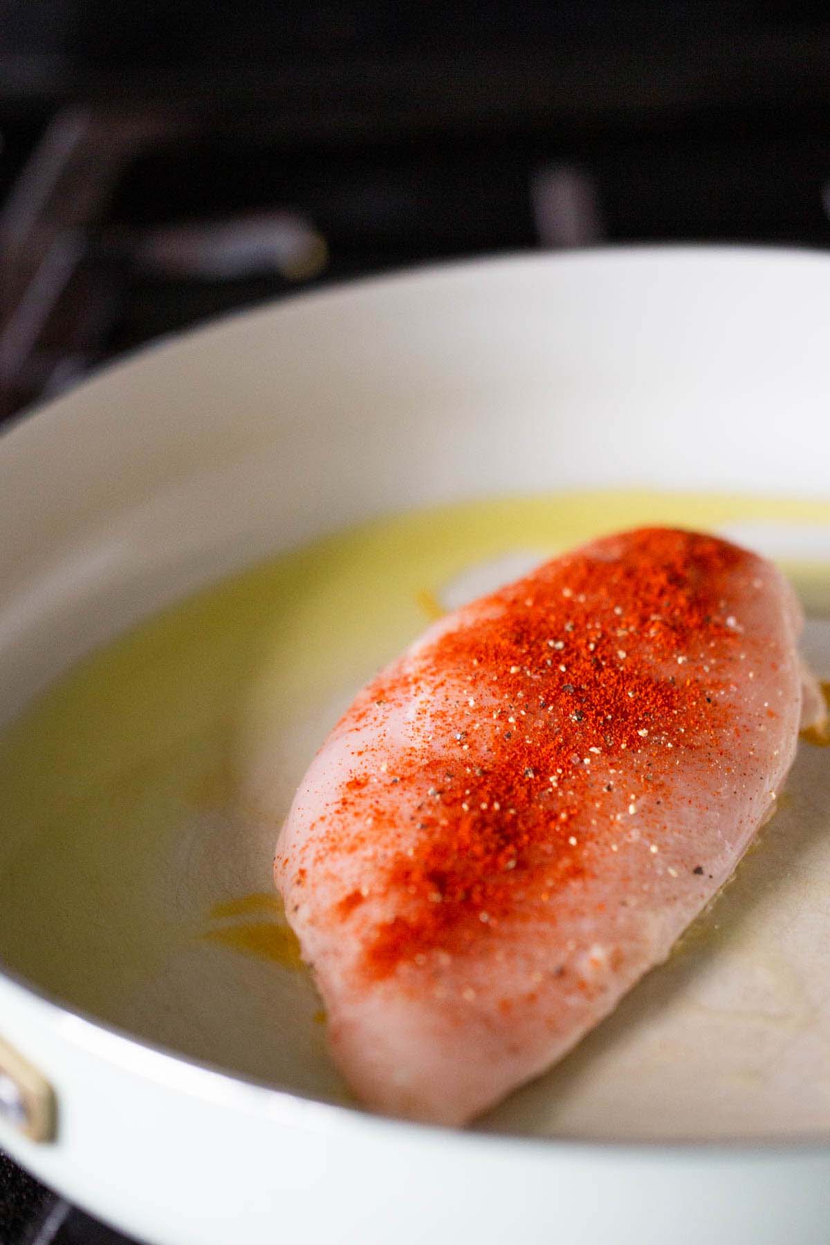 Chicken breast searing in a skillet.