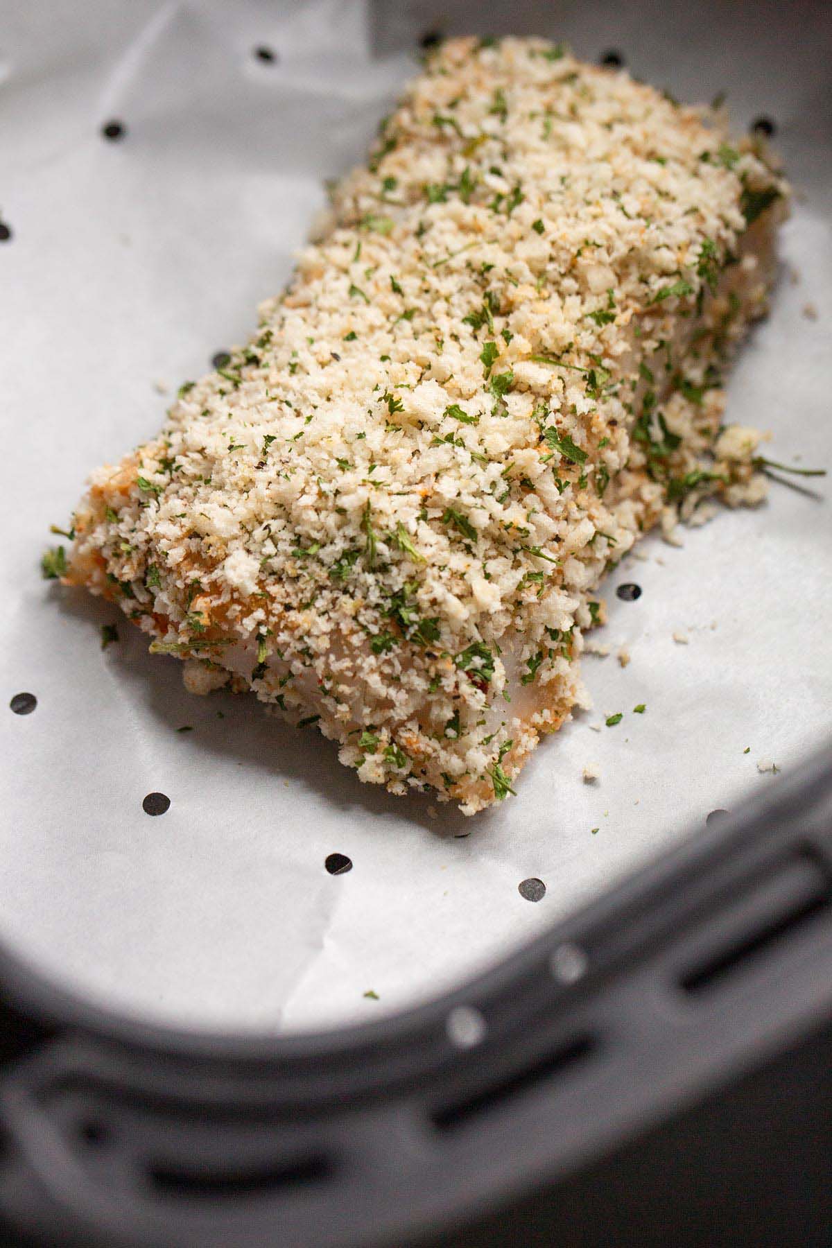 Uncooked panko cod in air fryer basket.