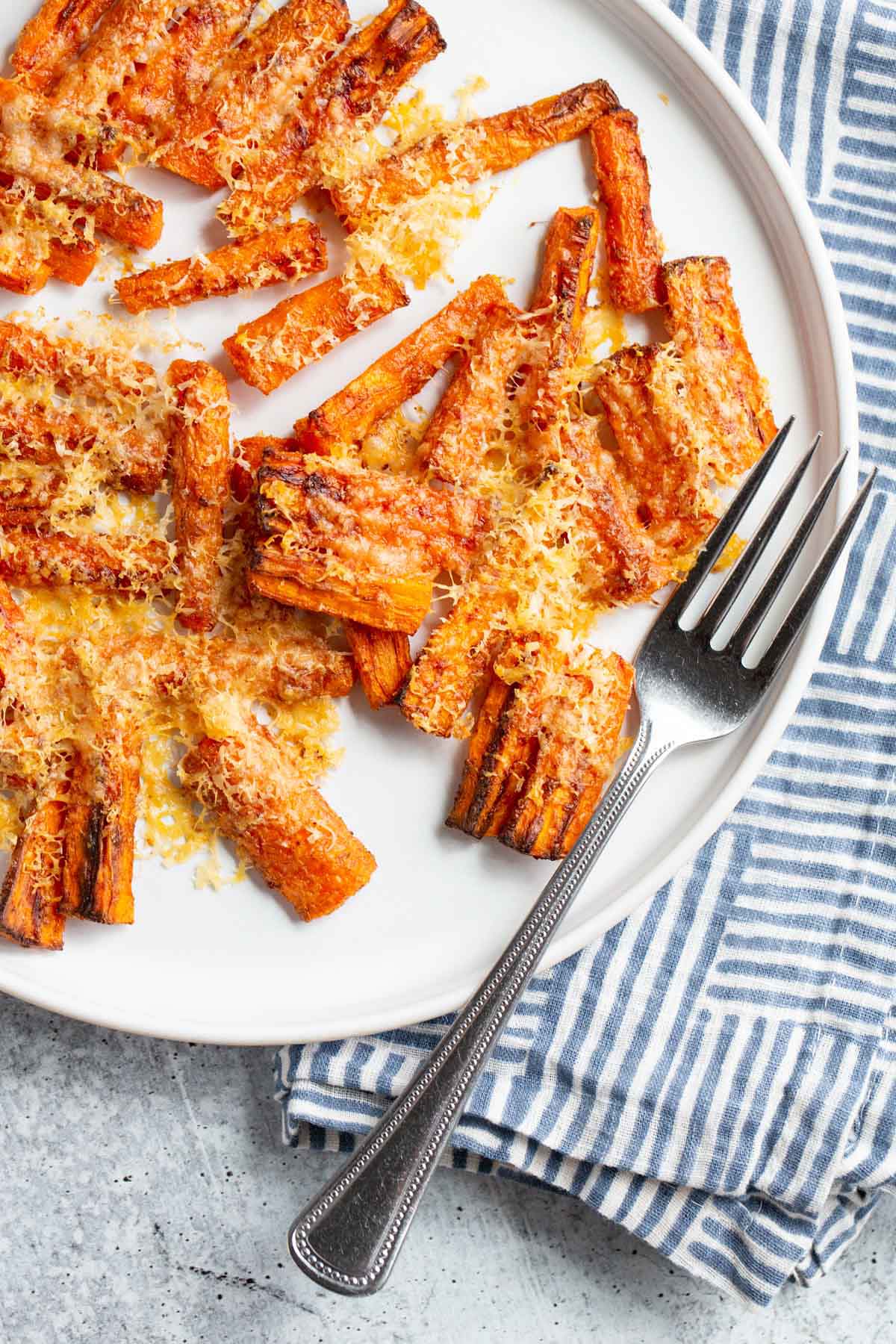 Parmesan carrots on a white plate with a blue and white napkin on the side.