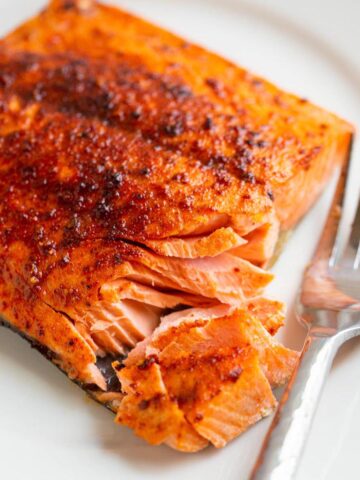 Air Fryer Sockeye Salmon flaked on a plate with a fork on the side.