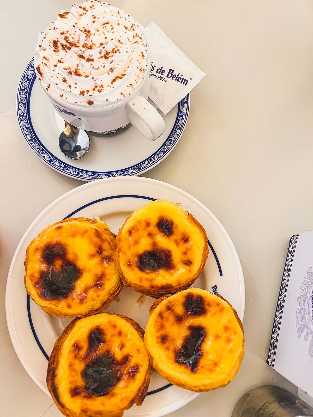 Pasteis de nata on a plate and cappuccinos with whipped cream.