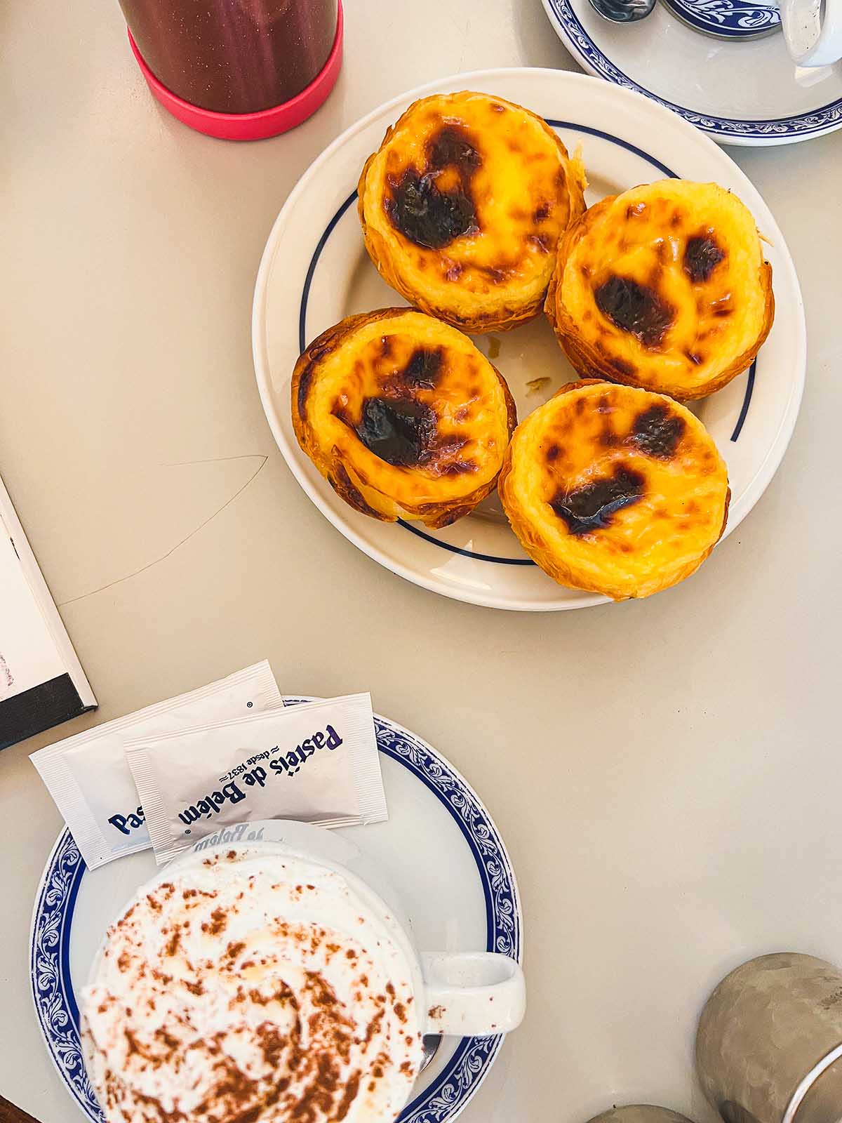 Pasteis de nata on a plate and cappuccinos with whipped cream.
