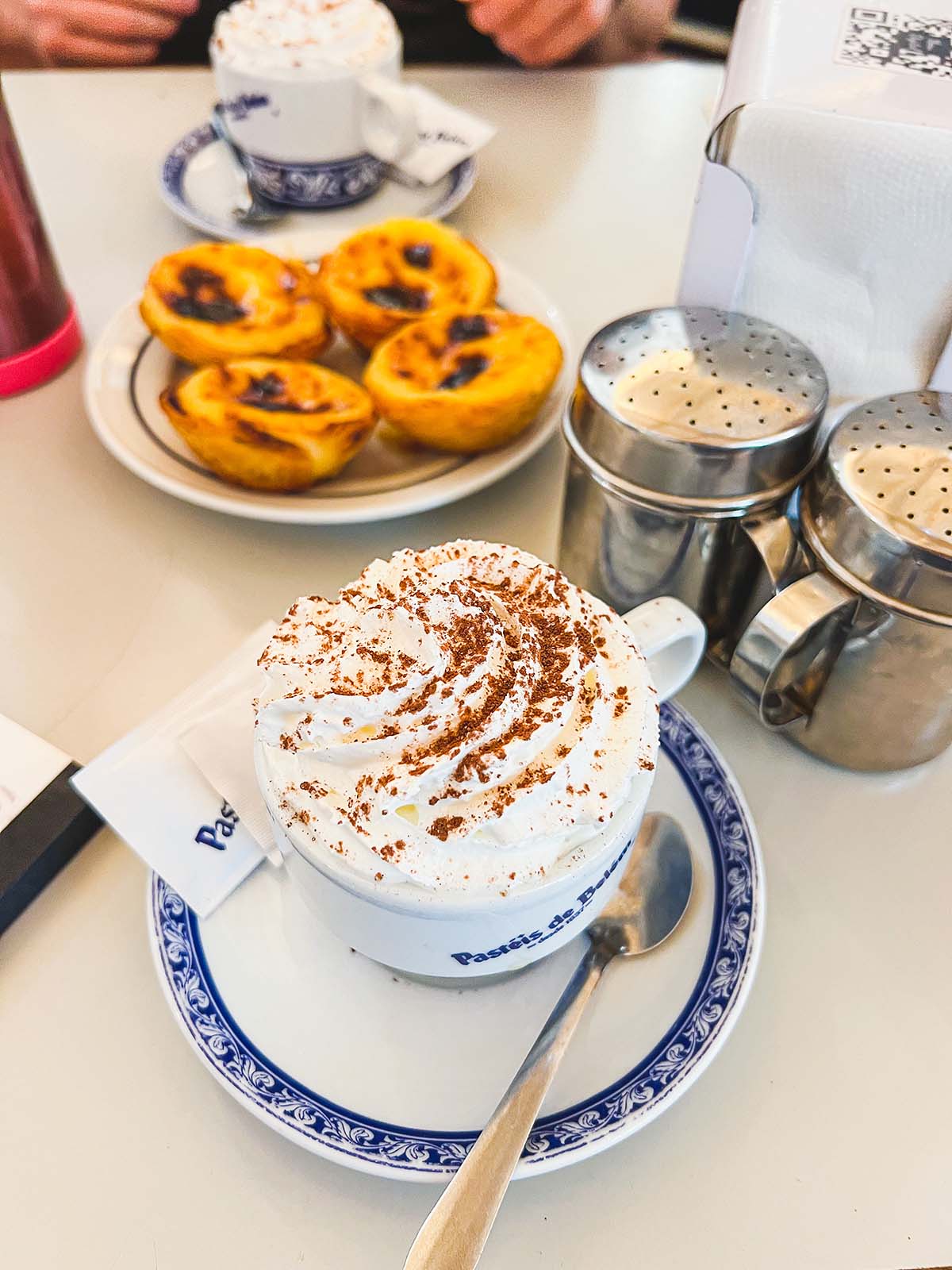 Pasteis de nata on a plate and cappuccinos with whipped cream.