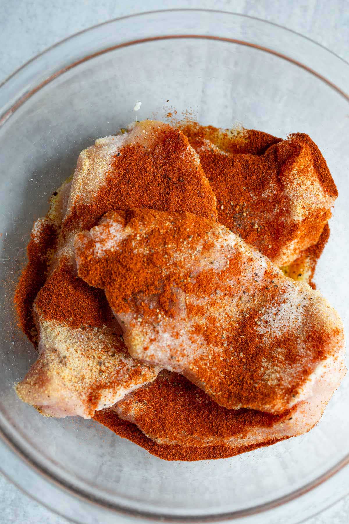 Pork chops with seasonings in a bowl.