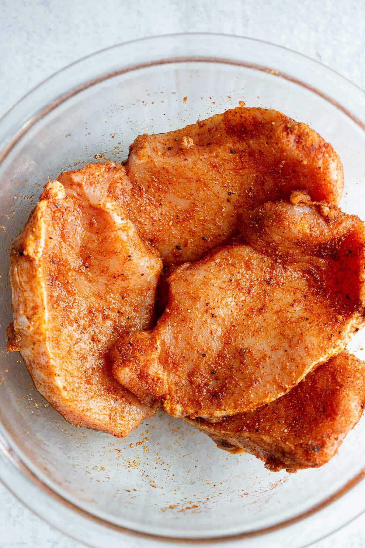 Pork chops with seasonings in a bowl.