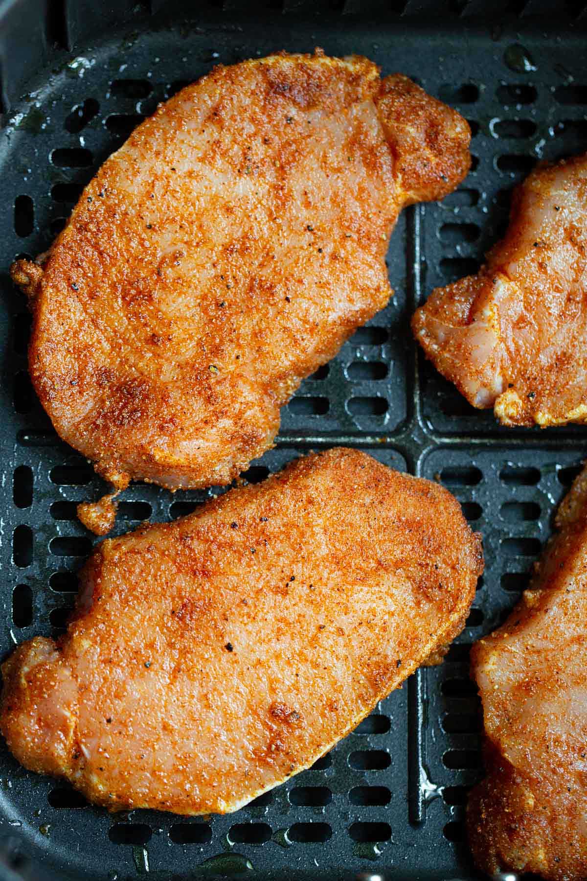 Uncooked pork chops in air fryer basket.