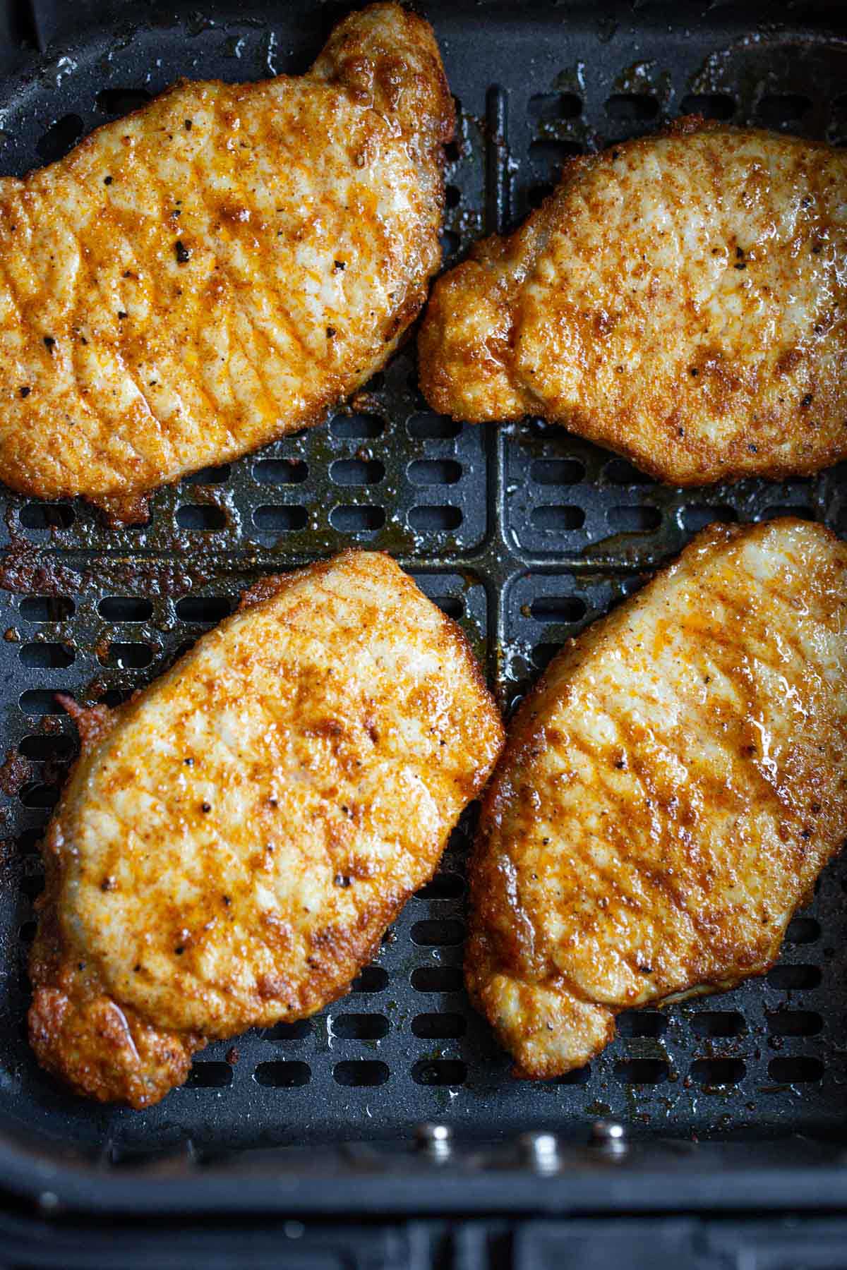 Cooked pork chops in air fryer basket.