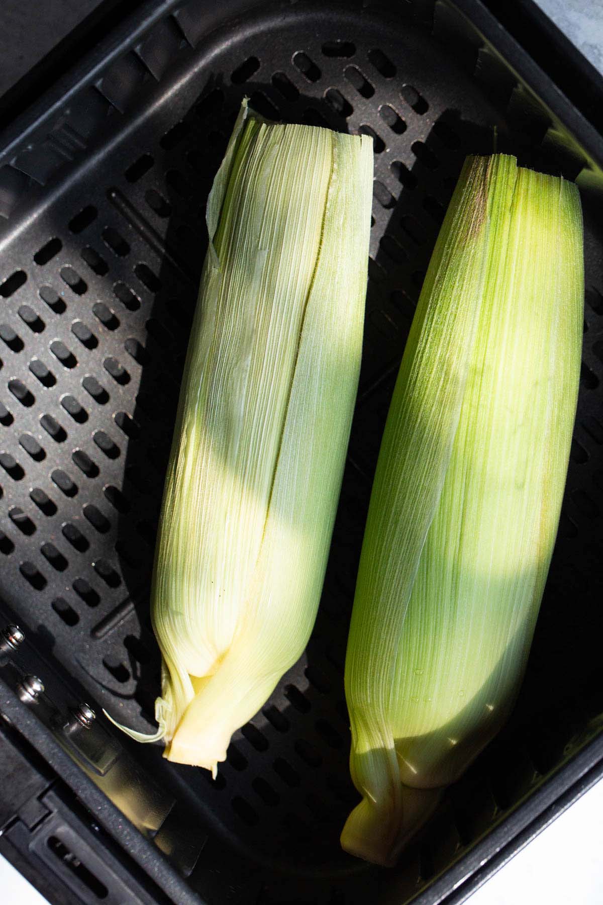 Uncooked corn on the cob in air fryer basket.