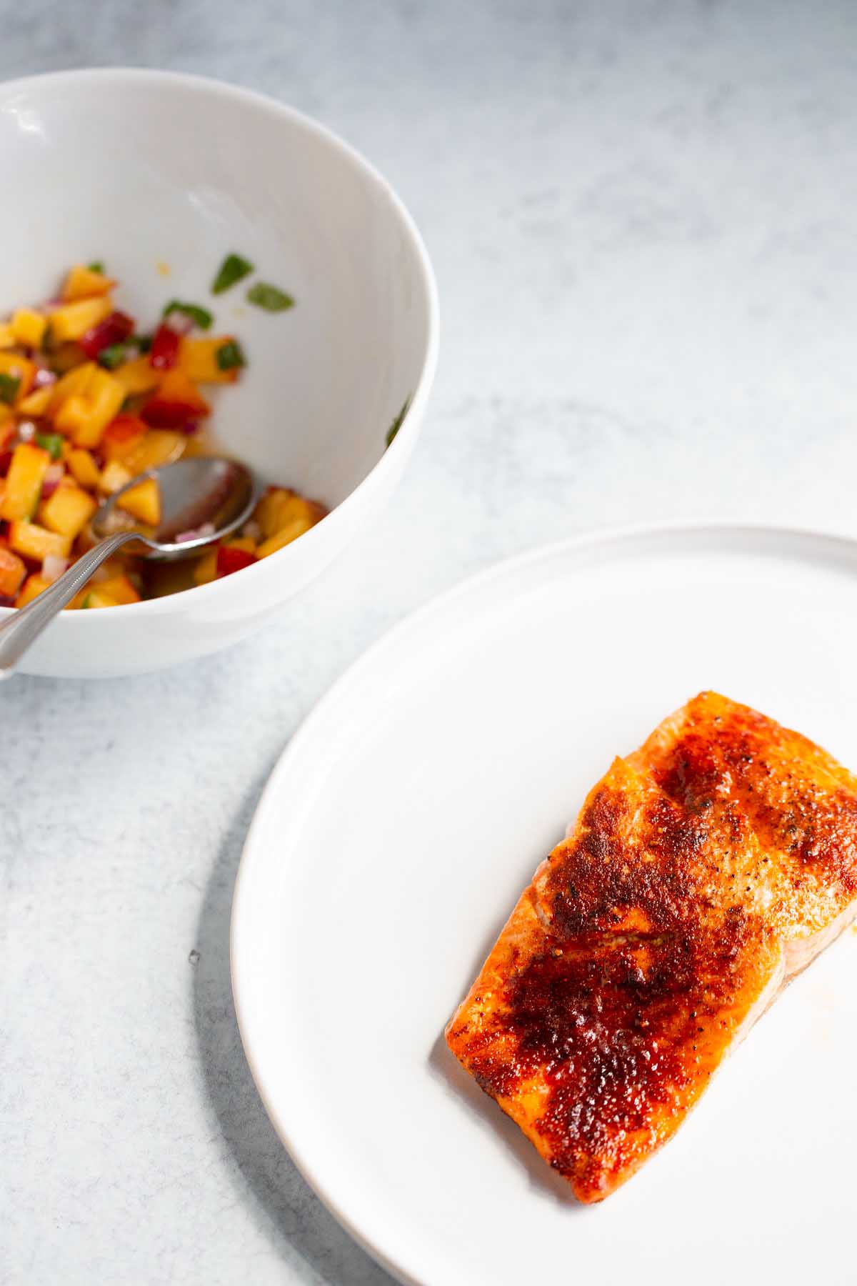 Salmon on a plate and peach salsa in a bowl.