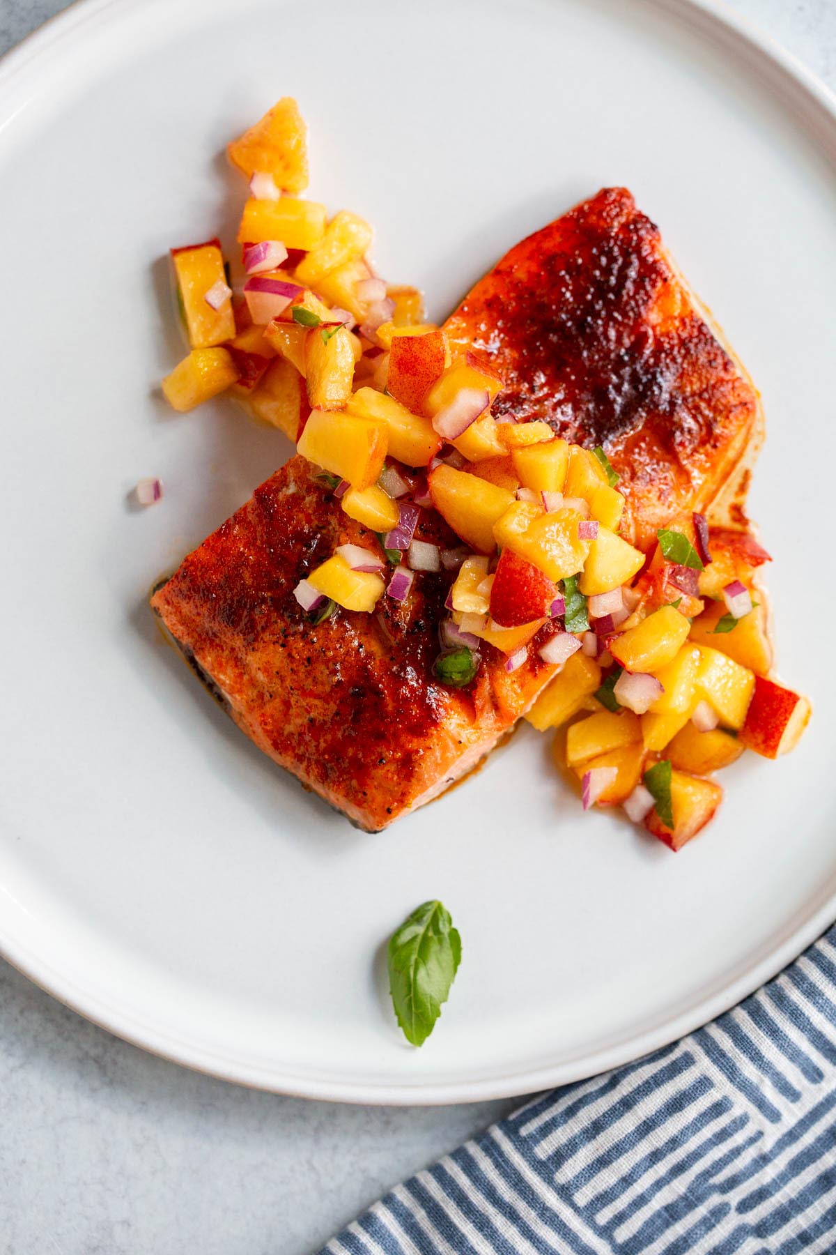 Air fried salmon on a white plate topped with peach salsa.