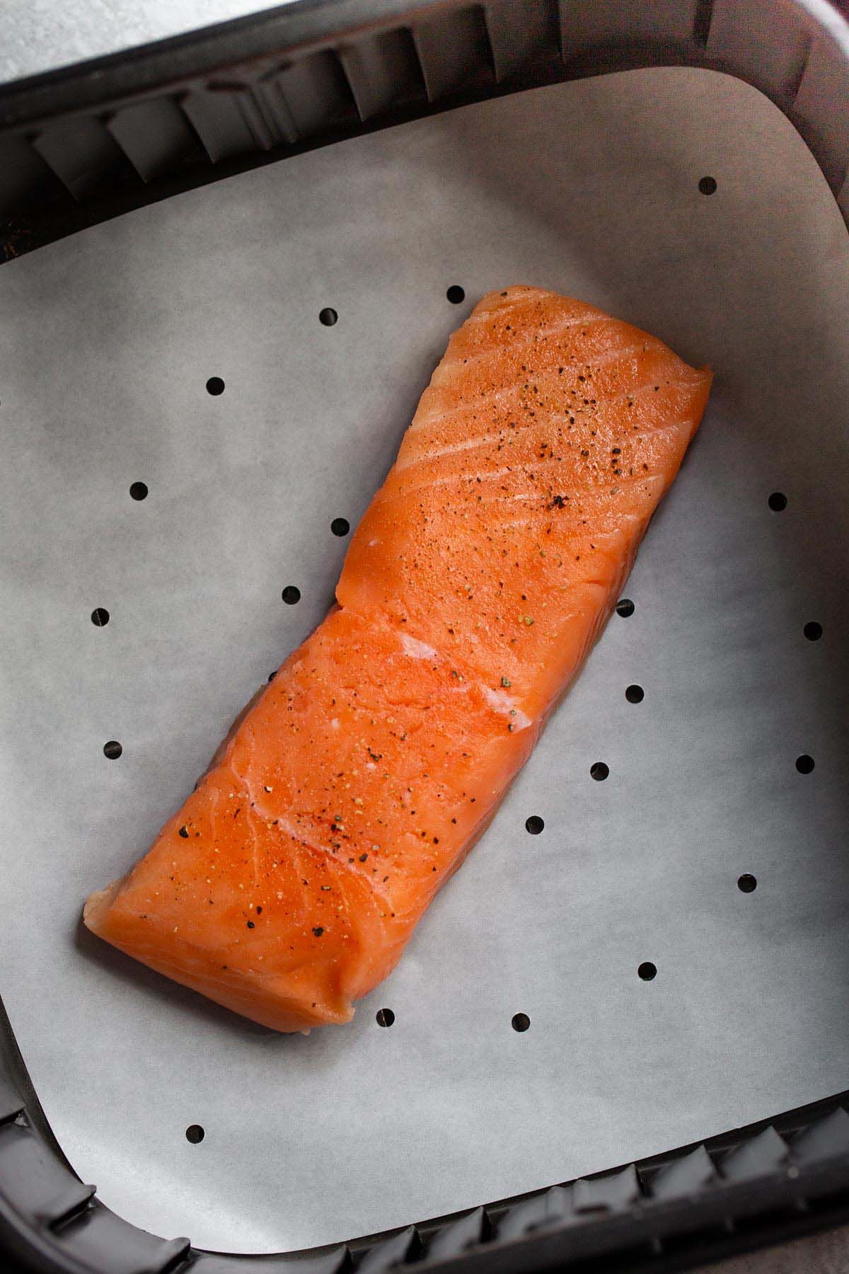 Uncooked salmon in air fryer basket.