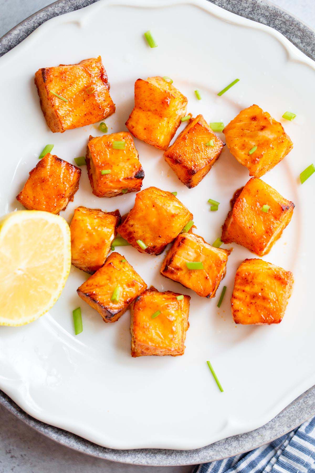 Salmon bites on a white plate with lemon on the side.