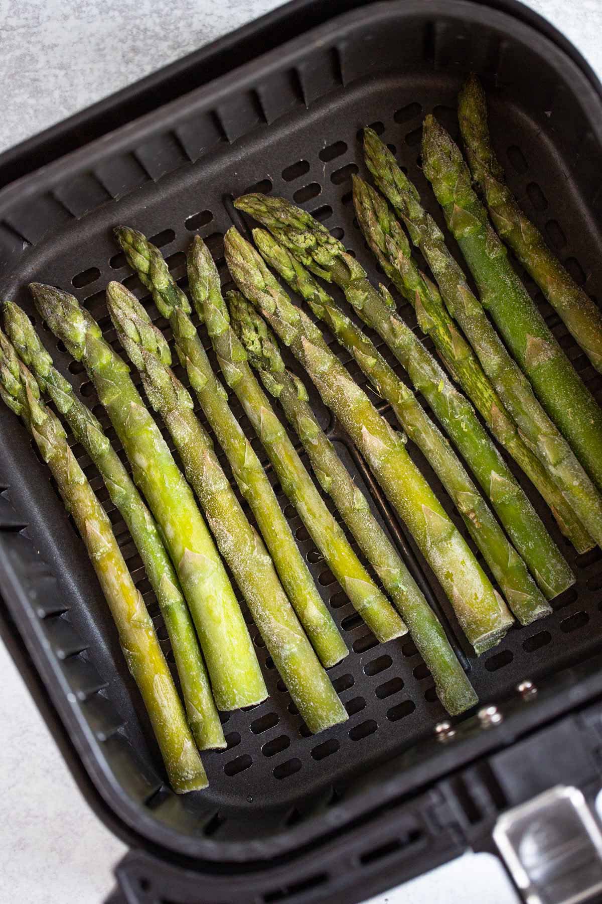 Frozen asparagus in air fryer basket.