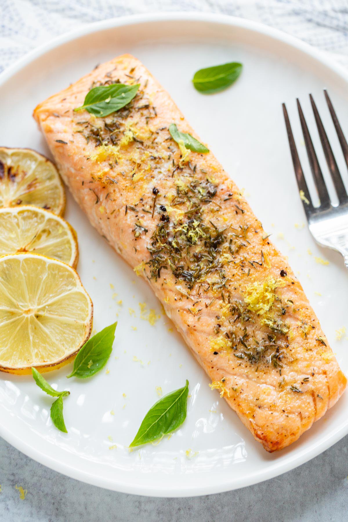 Air fried lemon garlic salmon on a plate with basil leaves.