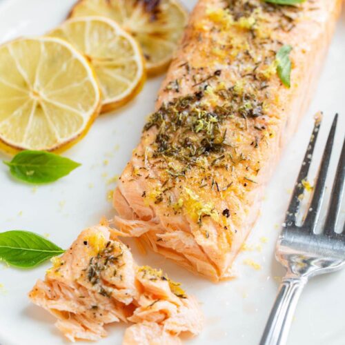 Air fried lemon garlic salmon on a plate with basil leaves.