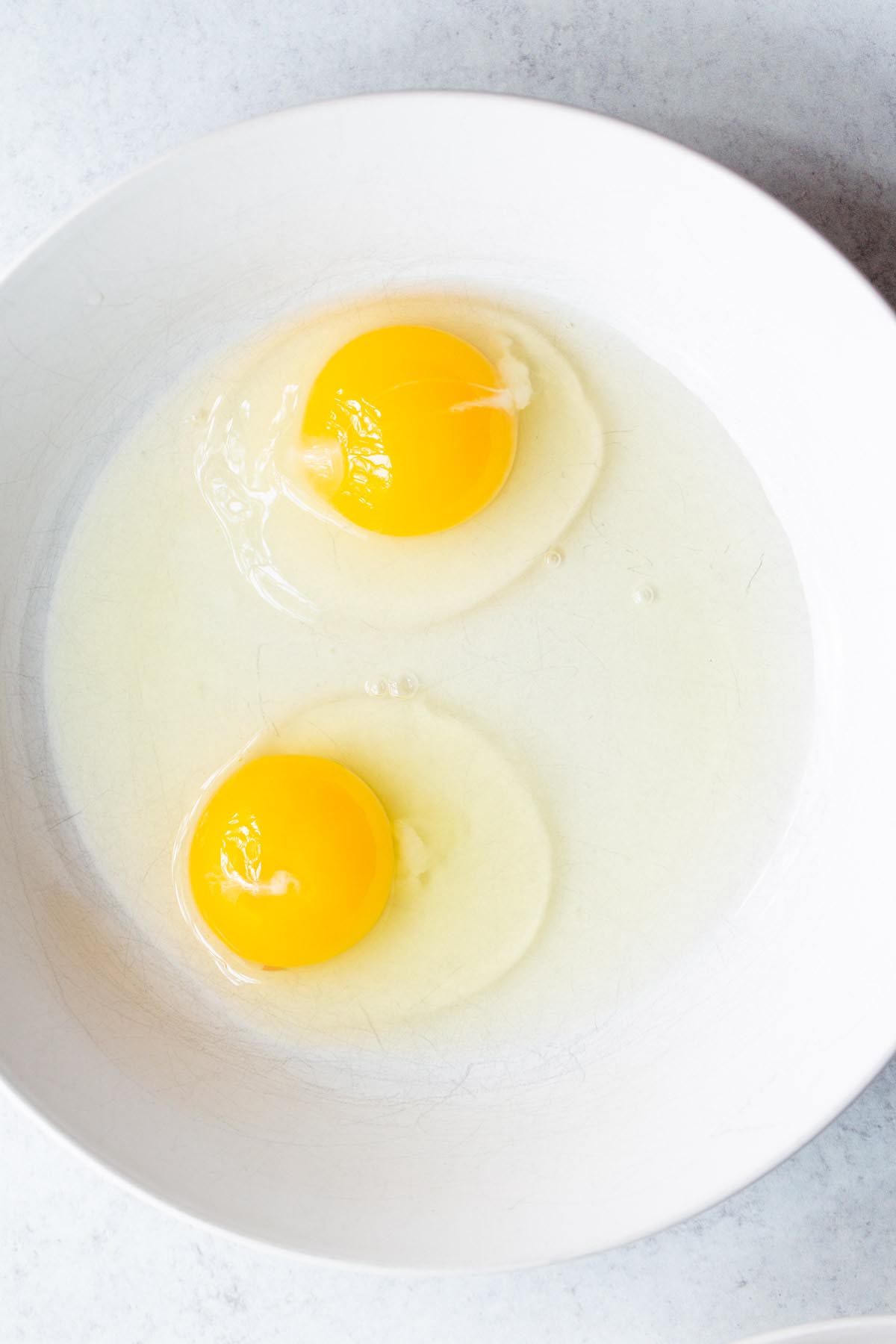 Two eggs cracked in a white bowl.