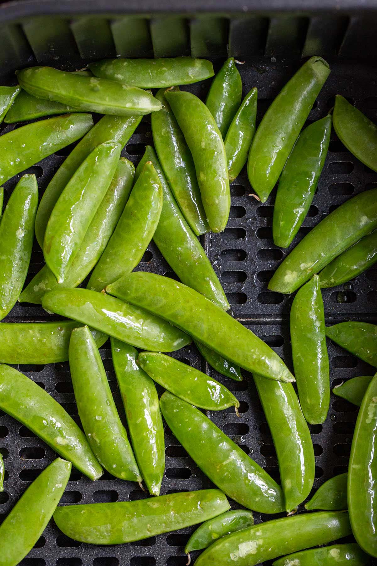 Uncooked snap peas in air fryer basket.