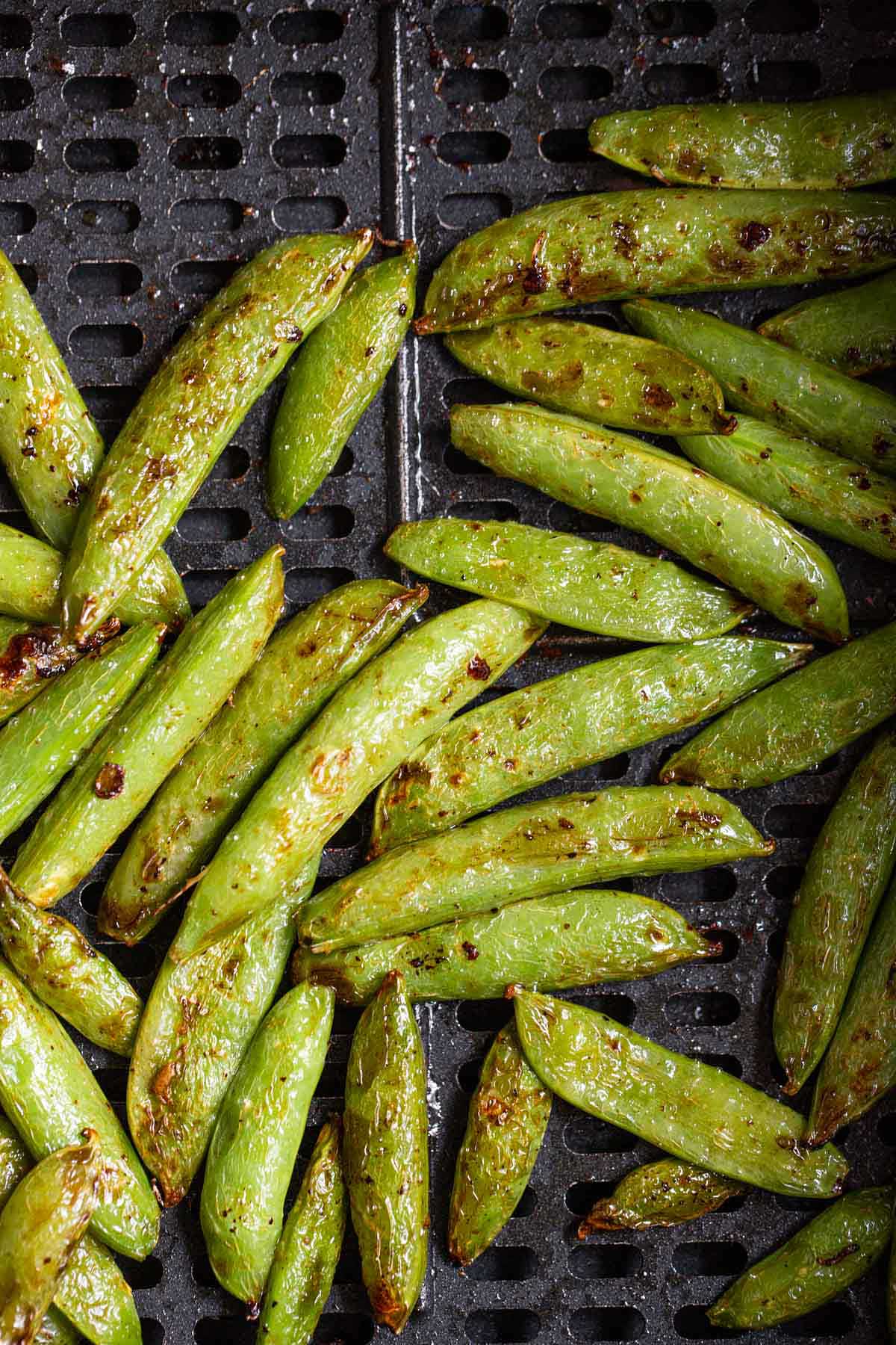 Cooked snap peas in air fryer basket.