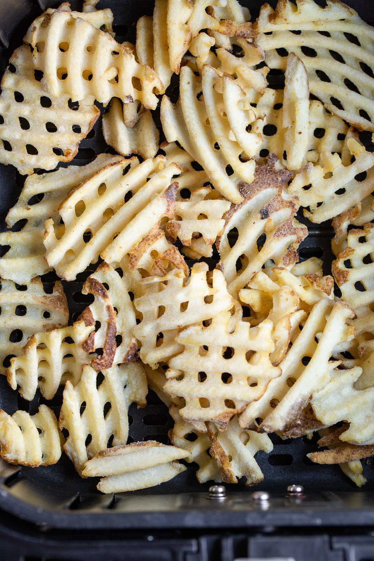 Uncooked waffle fries in air fryer basket.