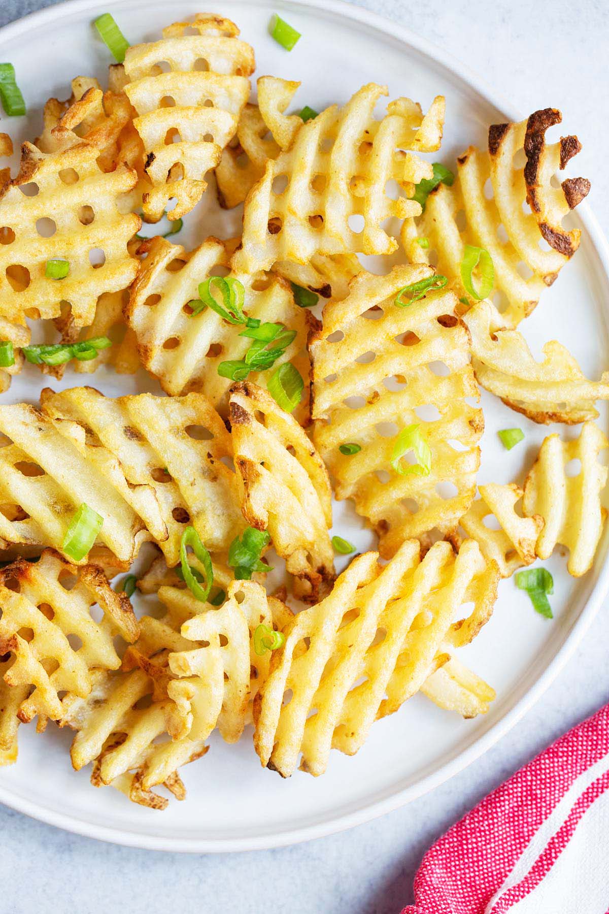 Waffle fries on a white plate with green onions.