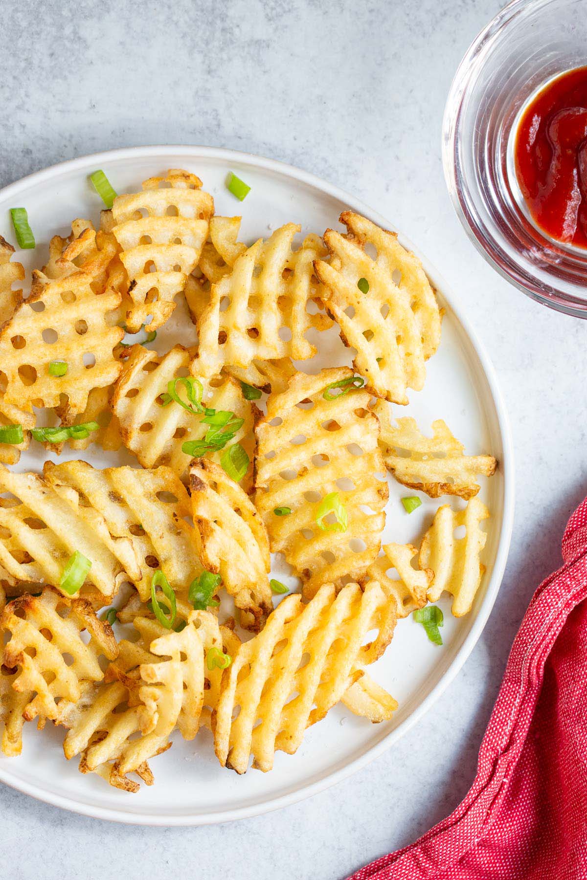 Waffle fries on a white plate with green onions.