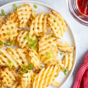 Waffle fries on a white plate with green onions.