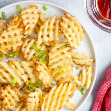 Waffle fries on a white plate with green onions.