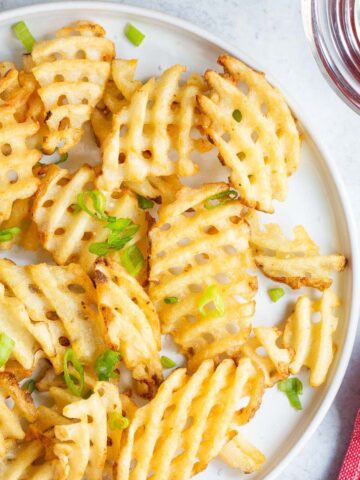 Waffle fries on a white plate with green onions.