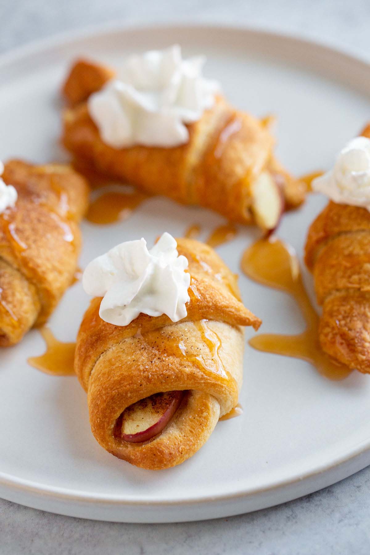 Apple pie crescent rolls on a plate with whipped cream.