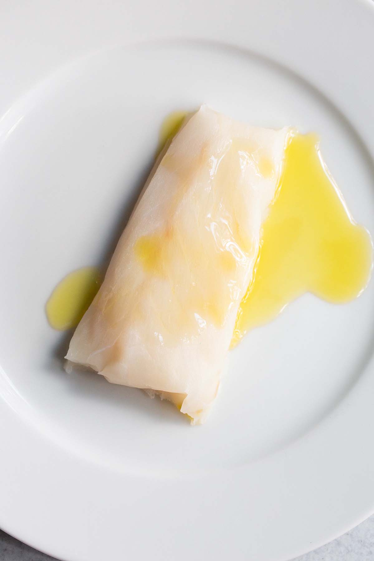 Uncooked cod with olive oil drizzled on top.