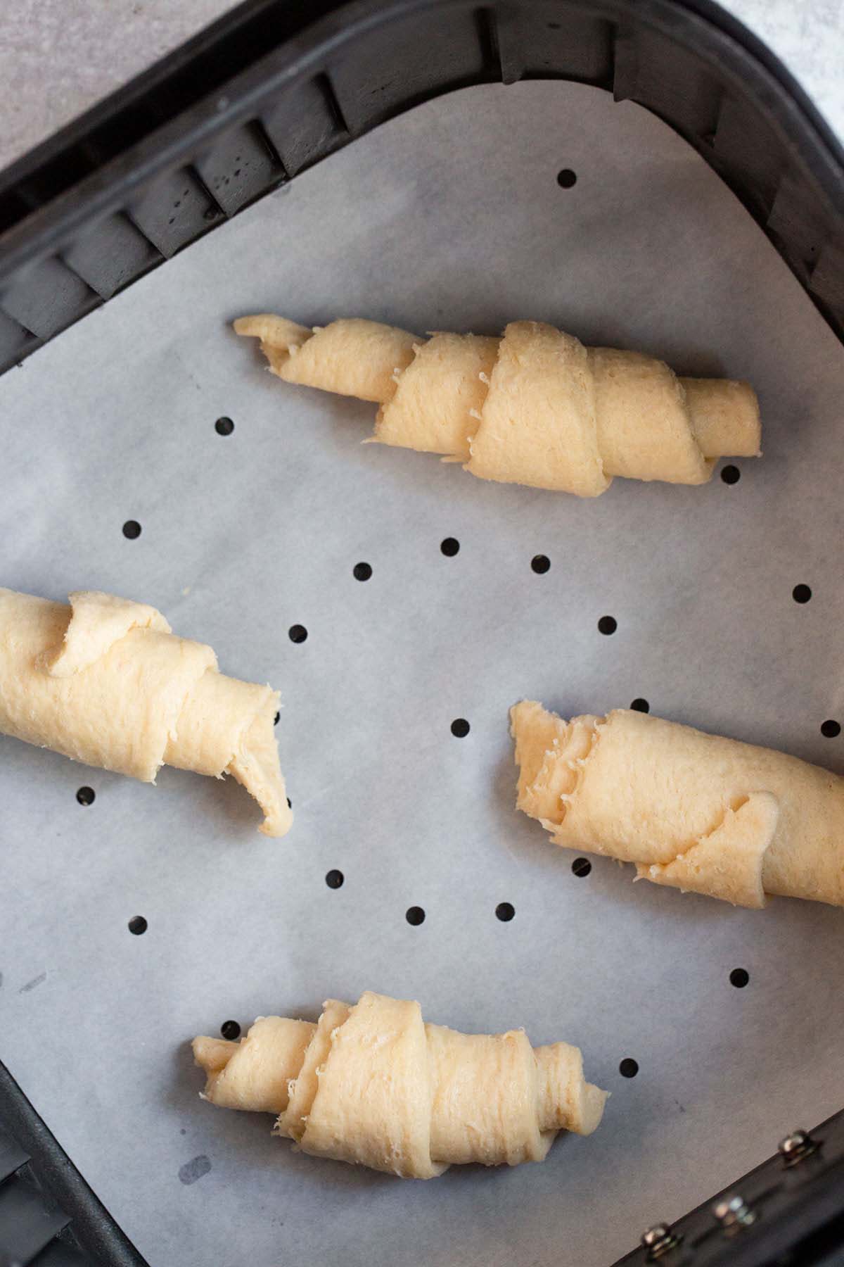 Uncooked crescent rolls in air fryer basket.