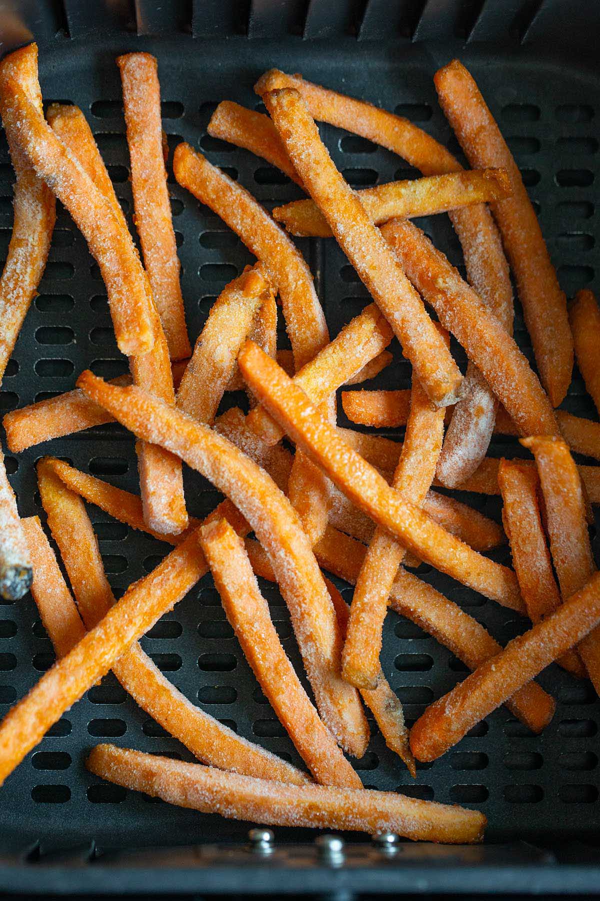 Frozen sweet potato fries in air fryer basket.