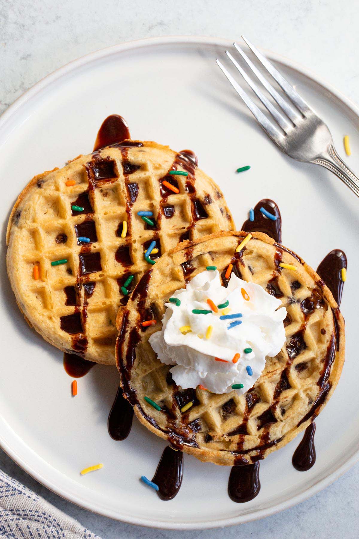 Waffles with whipped cream, chocolate syrup, and sprinkles.