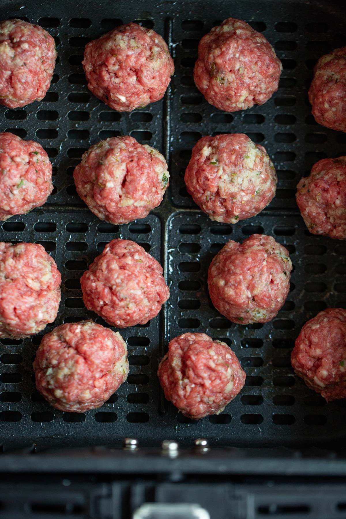 Uncooked meatballs in air fryer basket.