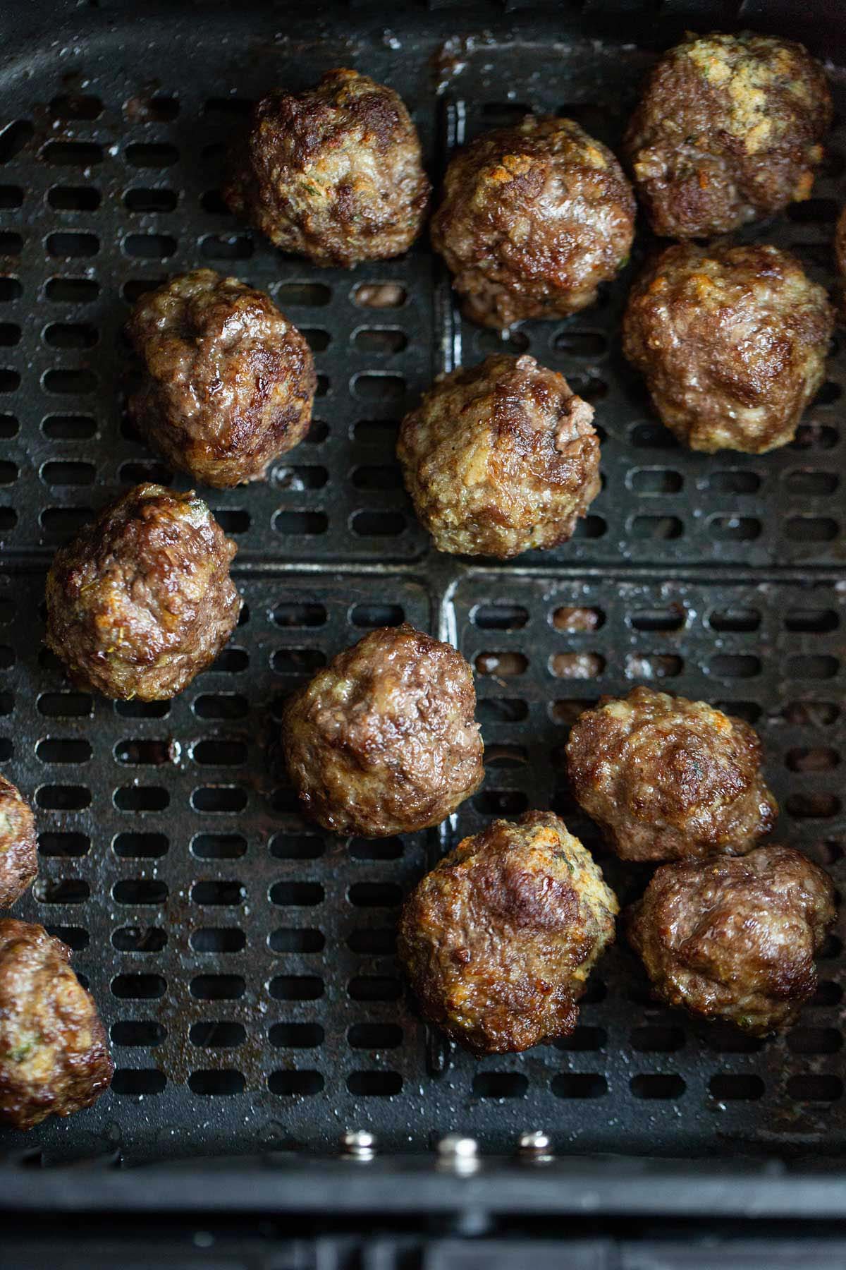 Cooked meatballs in air fryer basket.