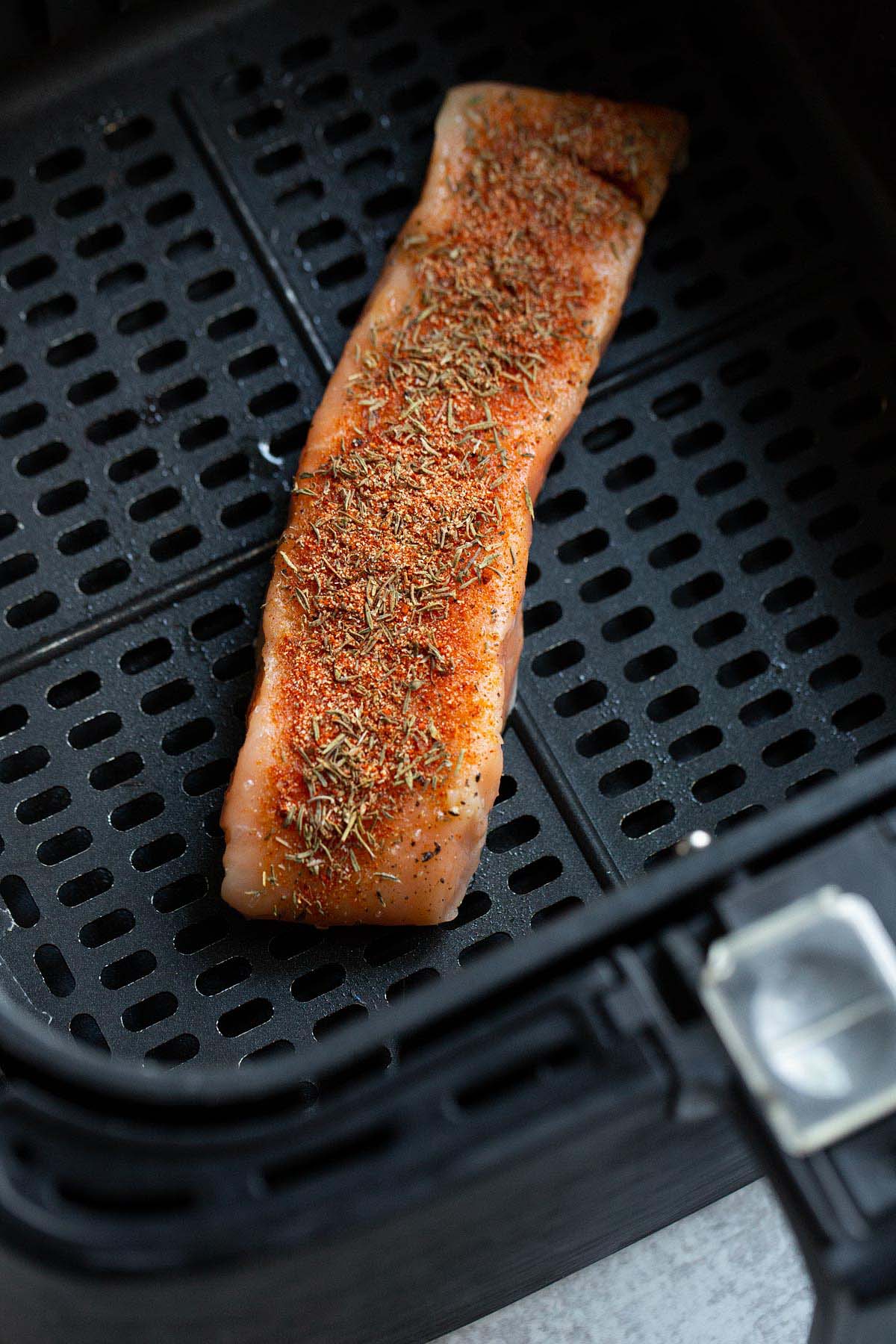 Uncooked salmon with spices in air fryer basket.