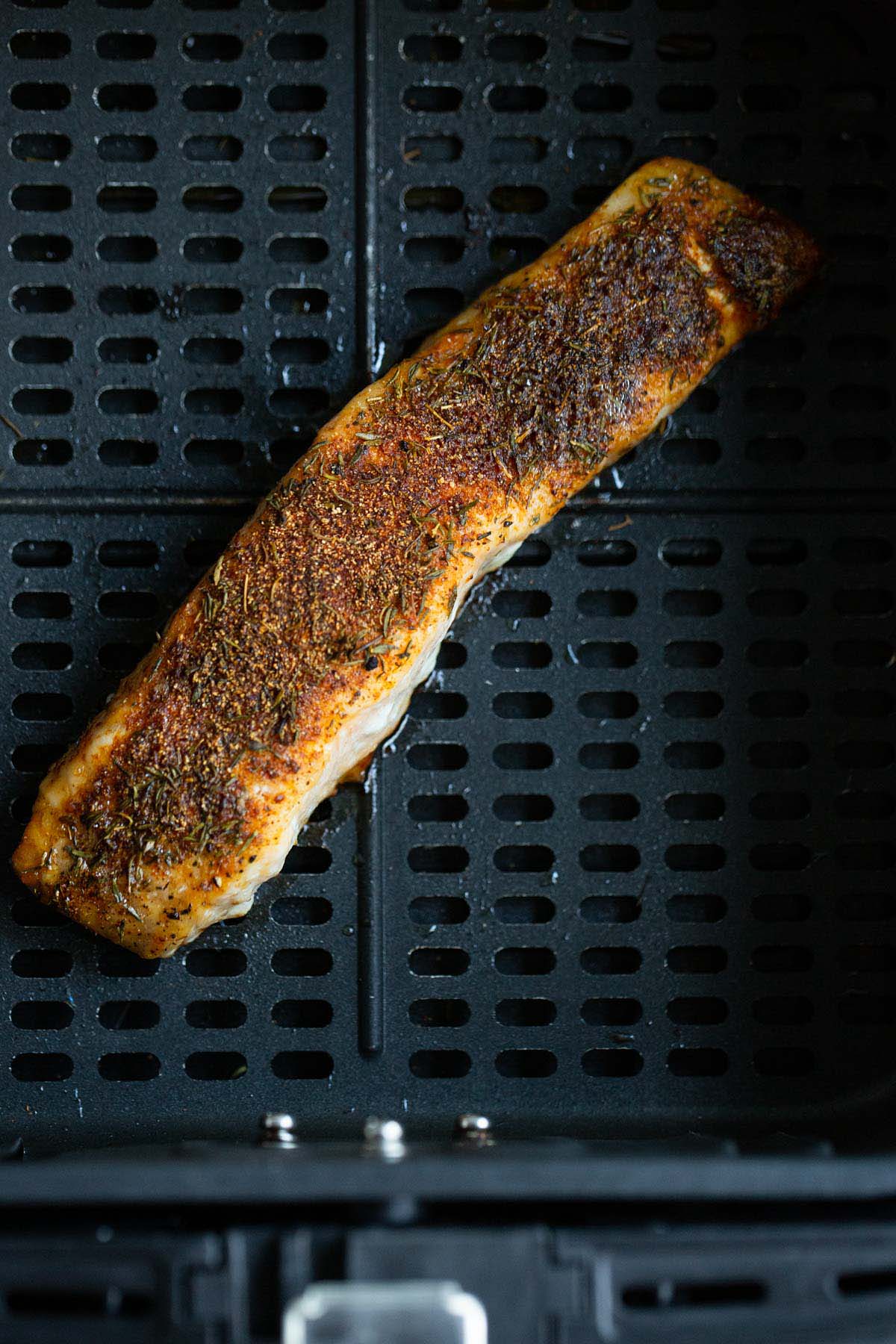 Cooked salmon with spices in air fryer basket.