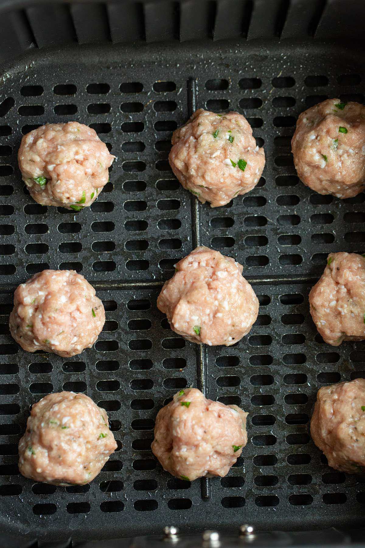 Raw meatballs in air fryer basket.