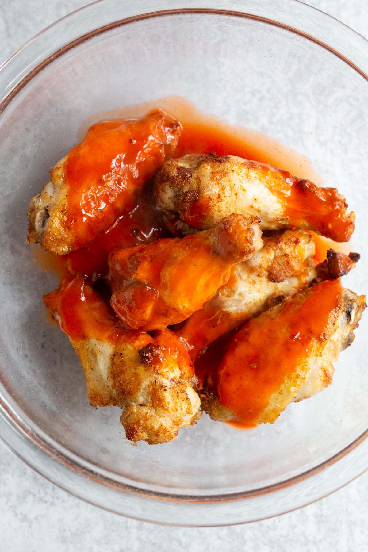 Wings in a bowl about to be tossed with buffalo sauce.