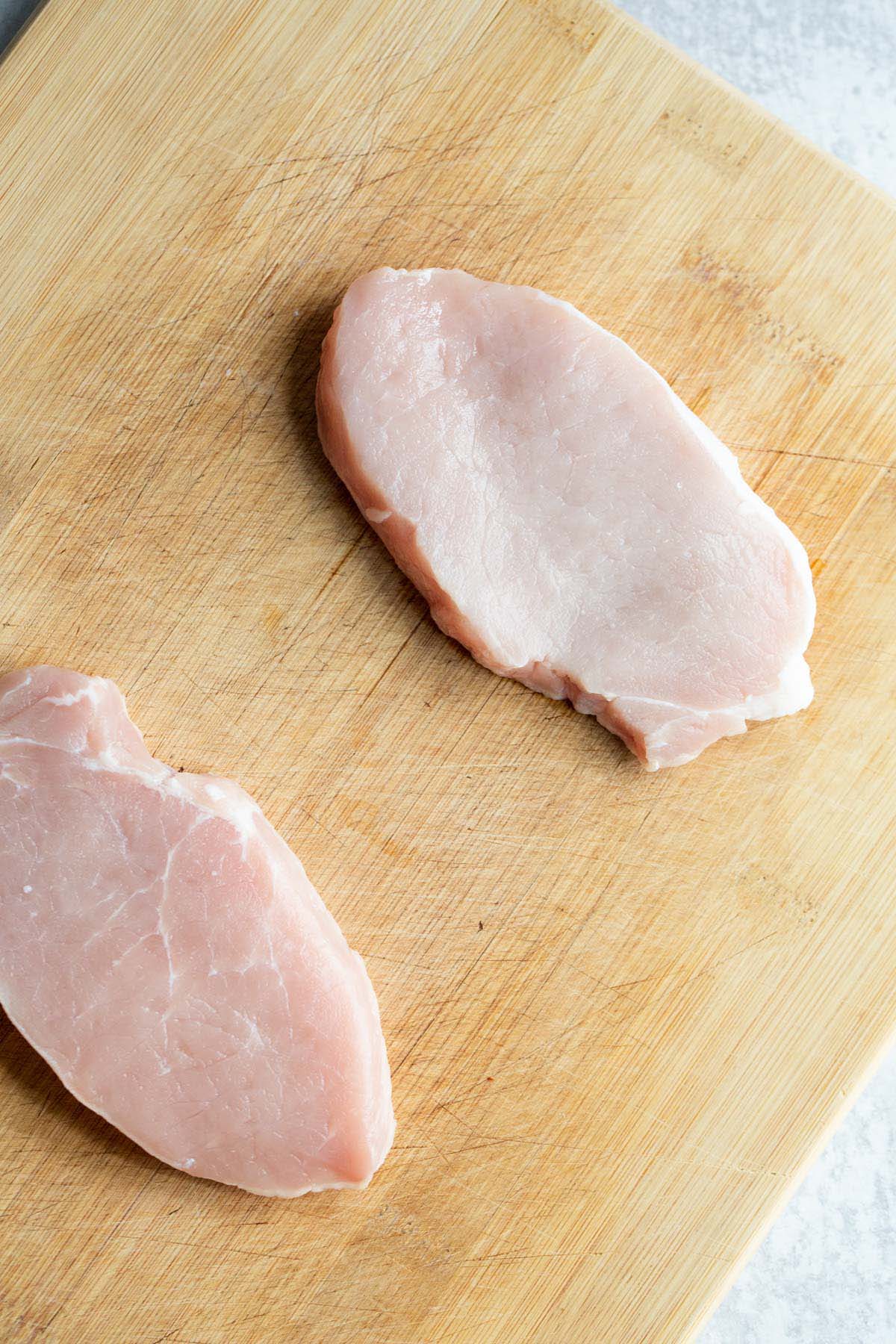 2 pork chops on a cutting board.