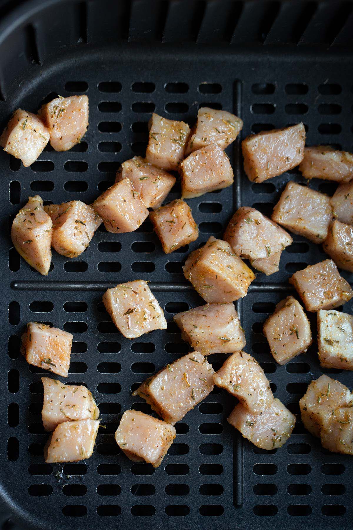 Raw cubed pork in air fryer basket.