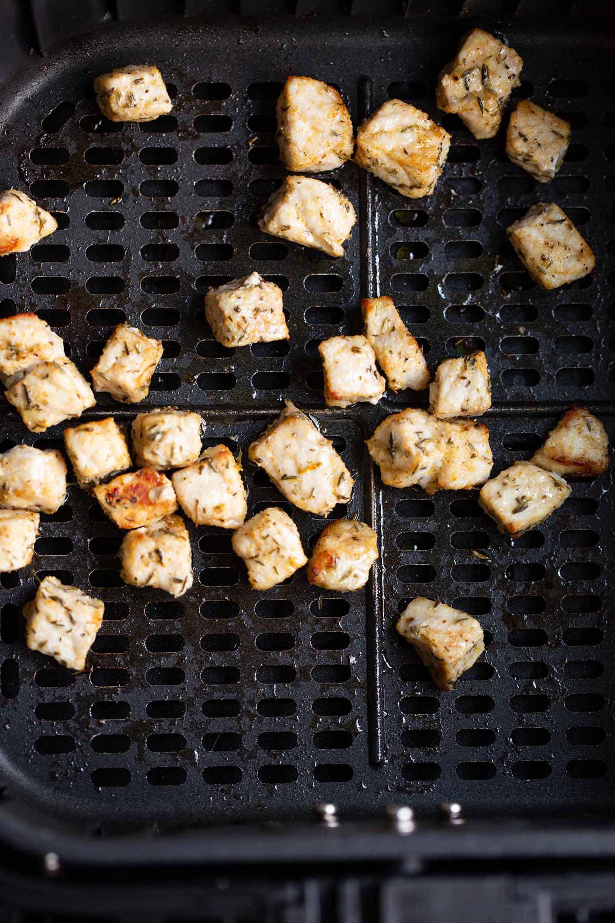 Cooked cubed pork in air fryer basket.