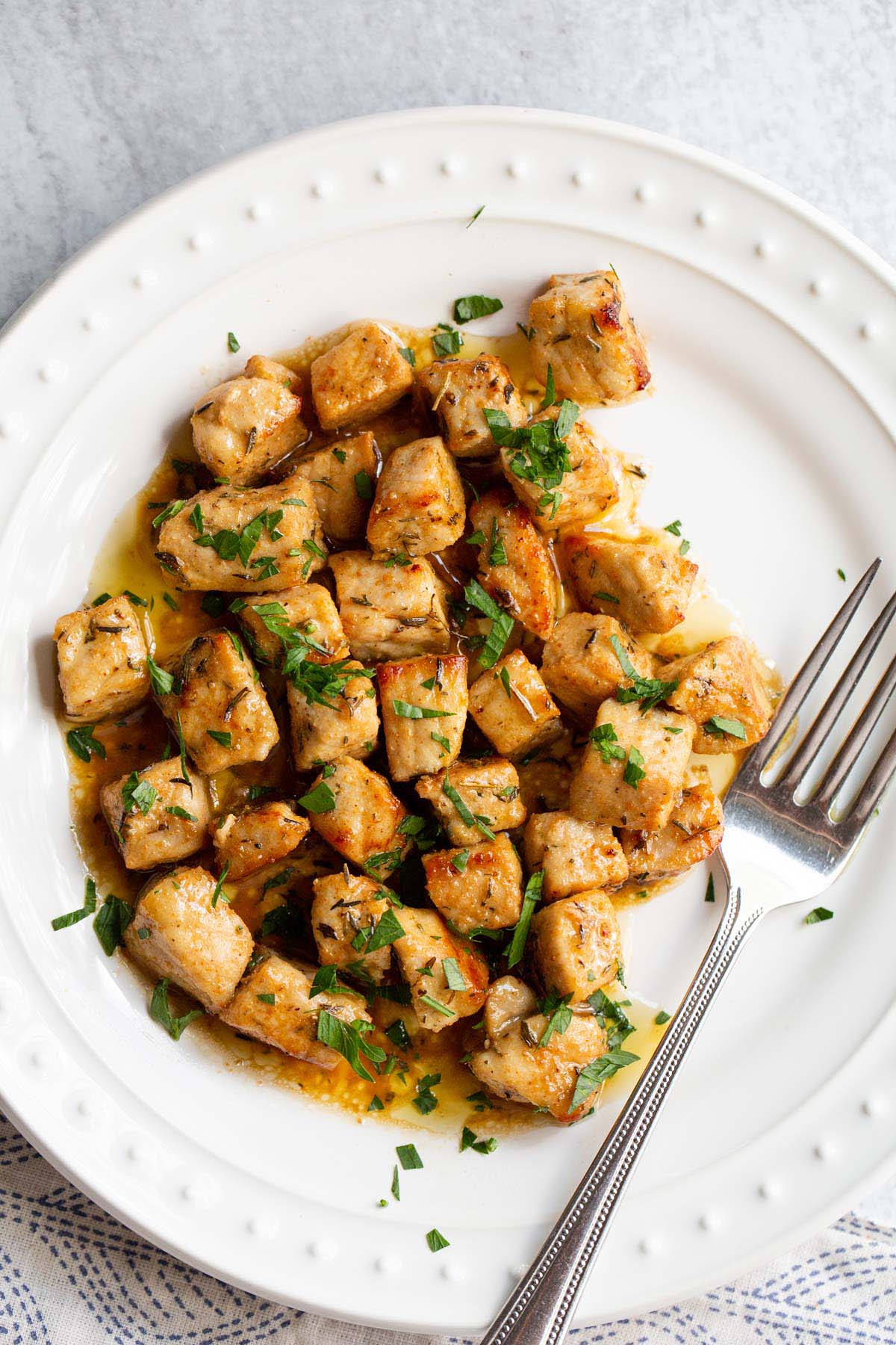 Air fried pork bites on a white plate with parsley garnish