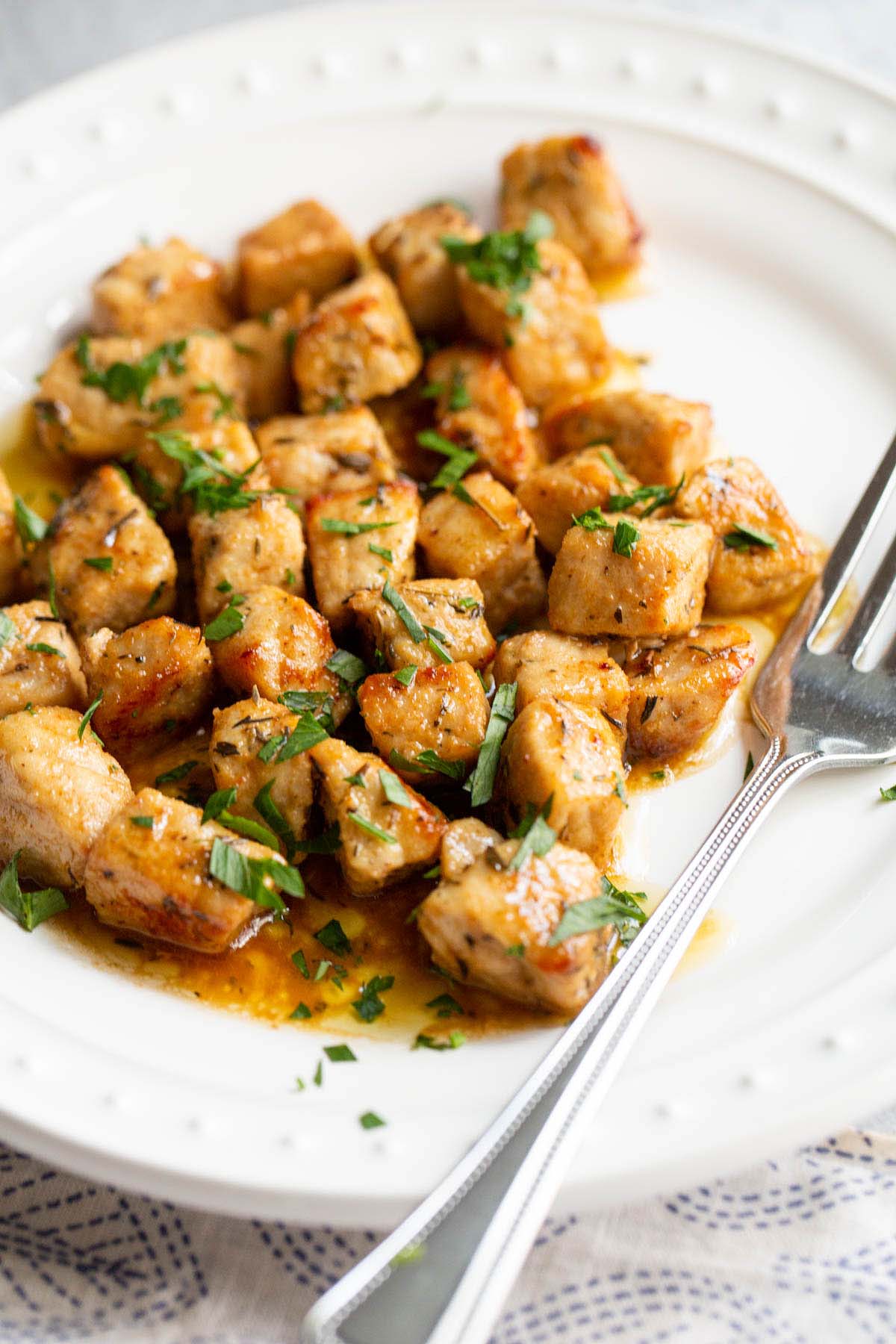 Air fried pork bites on a white plate with parsley garnish