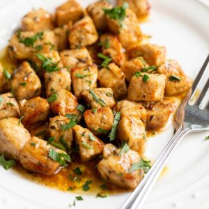 Air fried pork bites on a white plate with parsley garnish