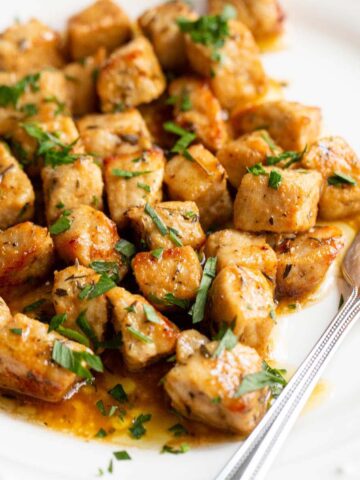 Air fried pork bites on a white plate with parsley garnish