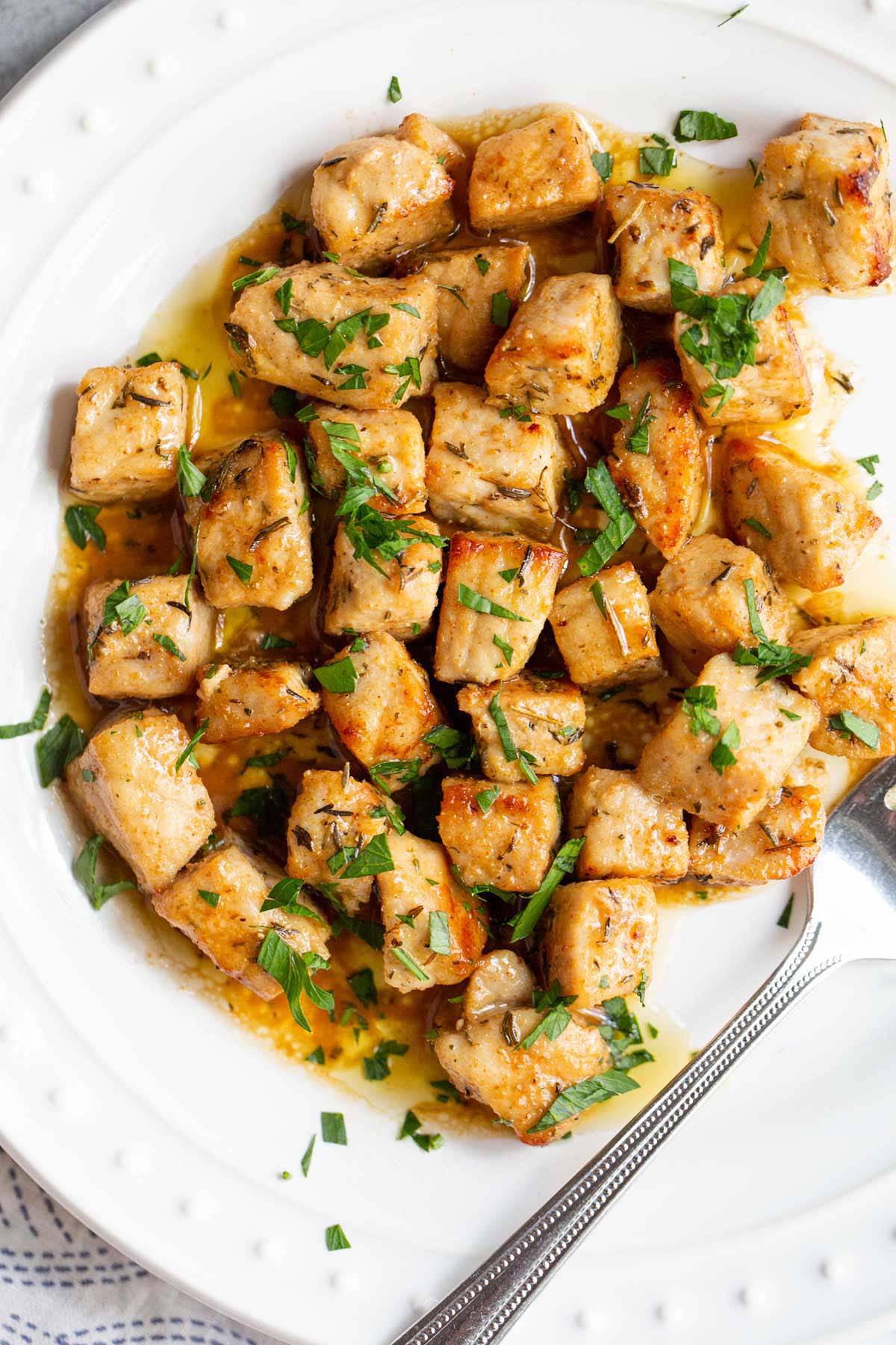 Air fried pork bites on a white plate with parsley garnish