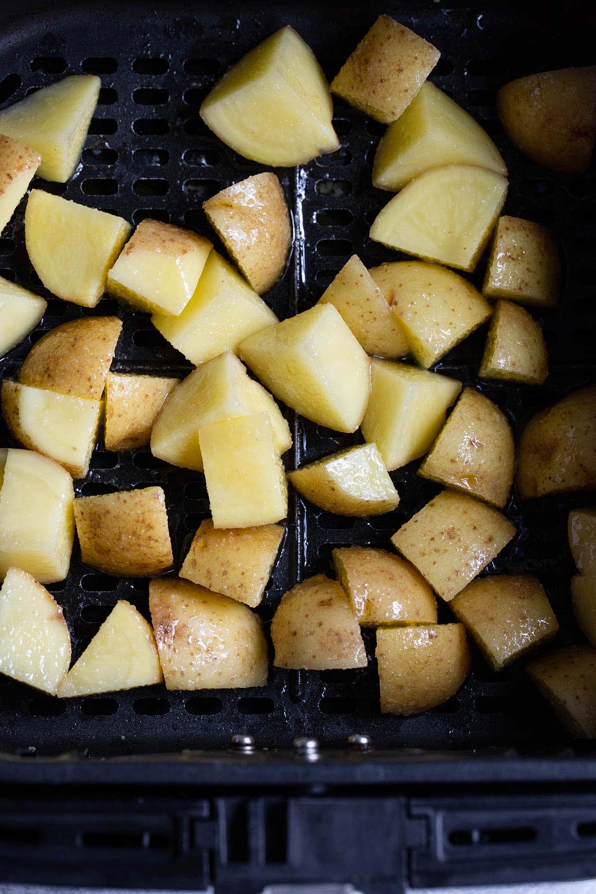 Uncooked potatoes in air fryer basket.