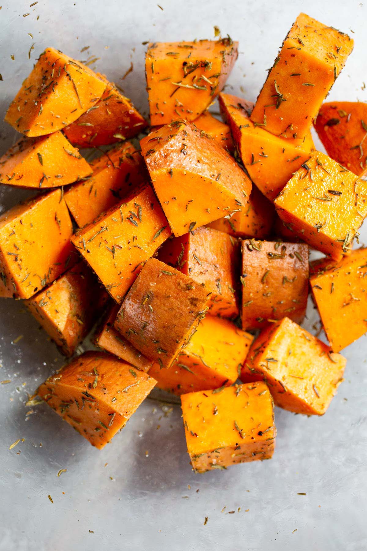Sweet potato cubes in a bowl tossed with oil and seasonings.